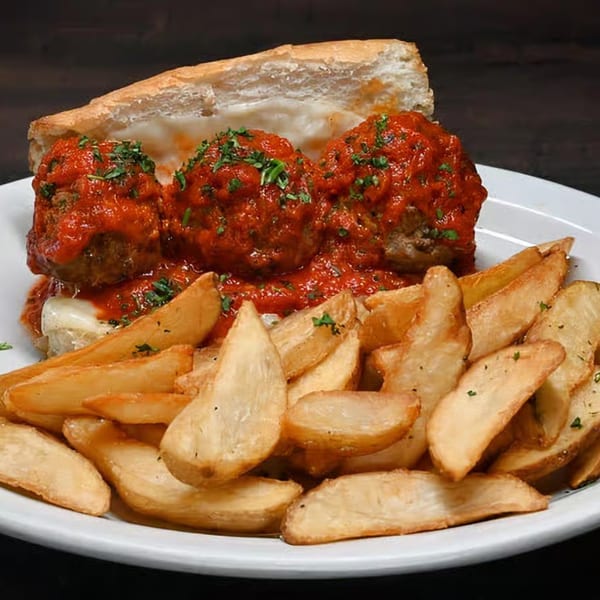 Meatball sub with melted cheese and red sauce, served with a side of potato wedges.