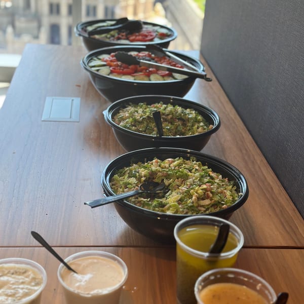 A buffet of salads and dressings from Leona's Pizzeria, with a city view in the background.