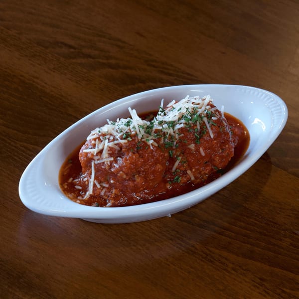 Two large meatballs covered in red sauce, grated cheese, and parsley in a white dish.