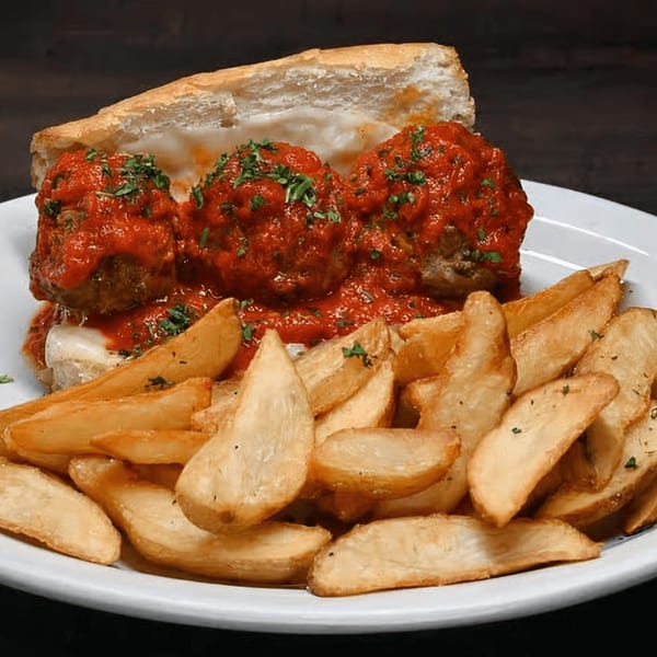 Meatball sub sandwich with melted cheese and red sauce, served with a side of potato wedges.