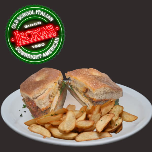 A Leona's Pizzeria sandwich, cut in half, with a side of potato wedges on a white plate.